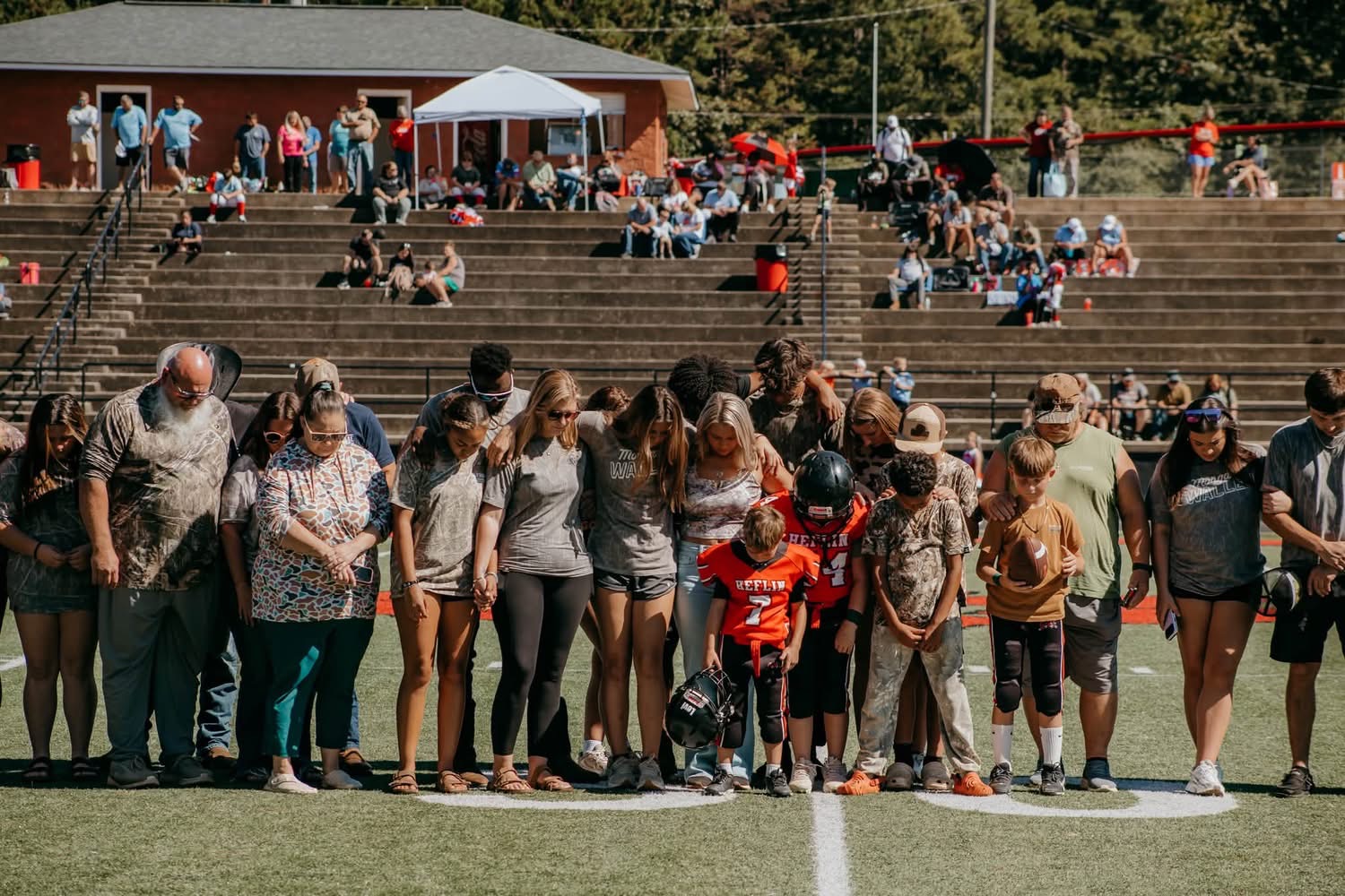 Family, players, and friends stand together across the football field during the tribute.